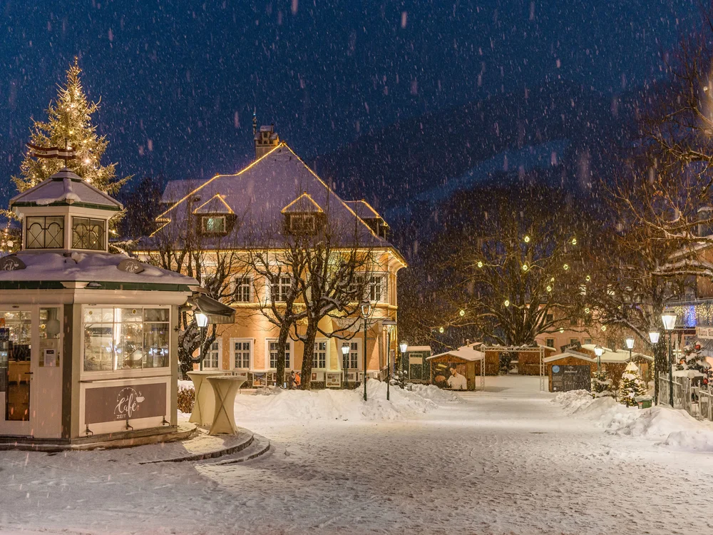 GRETI in Bad Hofgastein: dein alpines Boutique Hotel Verschneiter Dorfplatz bei Nacht mit beleuchtetem Weihnachtsbaum und Café-Kiosk