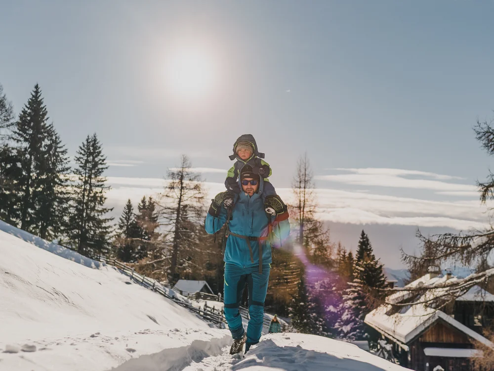 GRETI in Bad Hofgastein: dein alpines Boutique Hotel Mann mit Kind auf den Schultern geht durch eine verschneite Berglandschaft