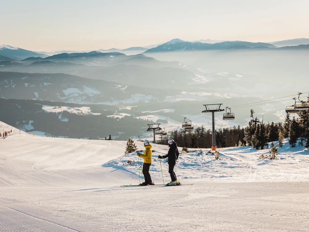 GRETI in Bad Hofgastein: dein alpines Boutique Hotel Zwei Skifahrer auf einer verschneiten Piste mit Sessellift und nebligen Bergen im Hintergrund