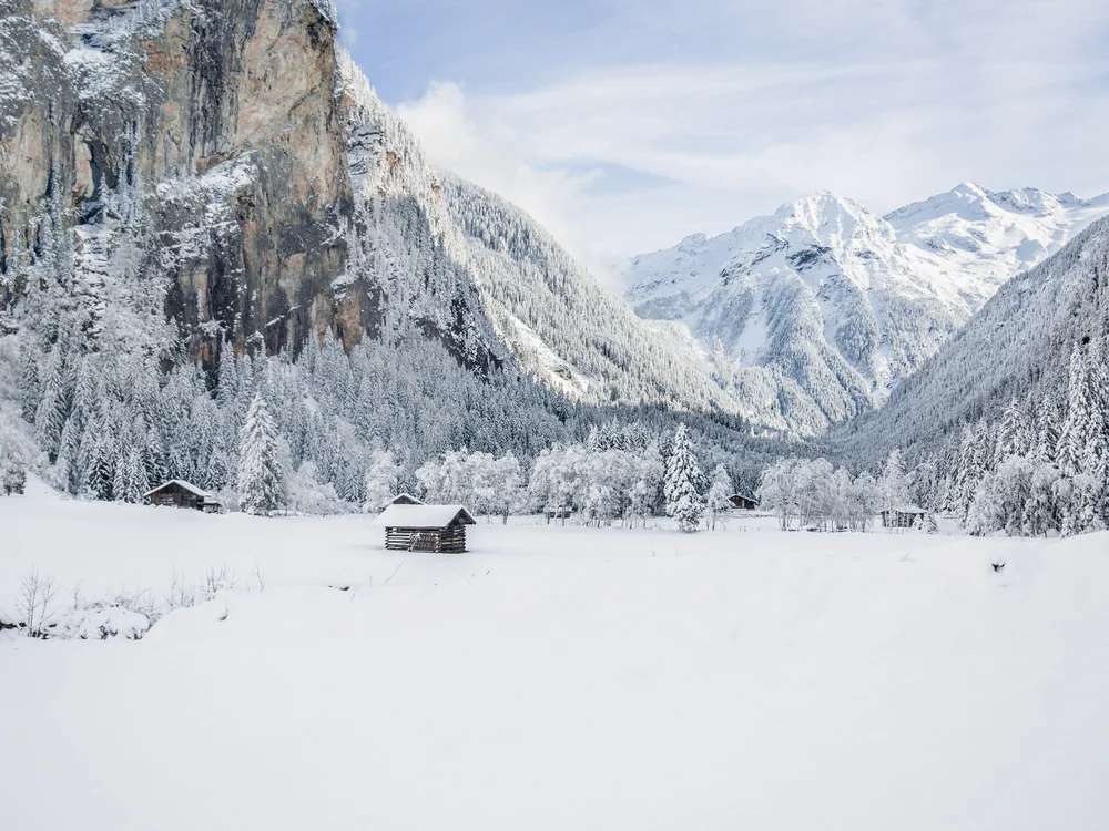 GRETI in Bad Hofgastein: dein alpines Boutique Hotel Verschneite Berglandschaft mit Holzhütten, Wald und schroffen Felswänden