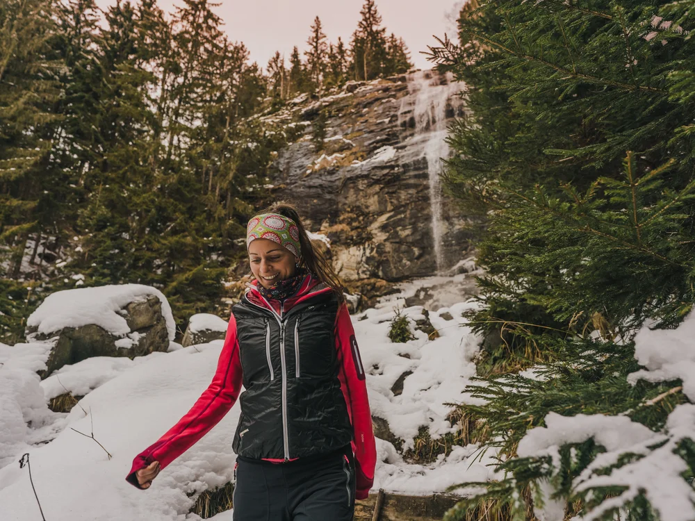 GRETI in Bad Hofgastein: dein alpines Boutique Hotel Lächelnde Frau in Winterkleidung an einem Wasserfall im verschneiten Wald